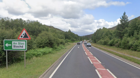 The A9 at Slochd. The road is single carriageway and there is a sign warning of the potential of rockfalls, another with the word "Slochd" in English and Gaelic.
