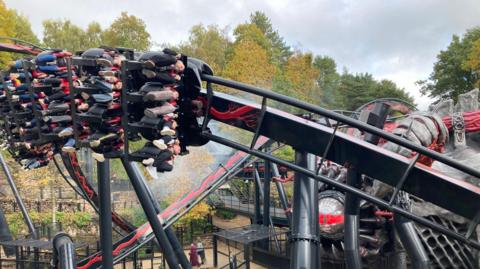 People riding a rollercoaster, their legs dangling underneath the carriage as it speeds at an angle round the track