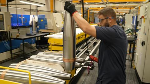Man holding a shell casing in a BAE factory