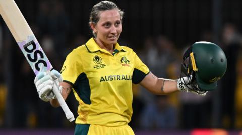 Ash Gardner takes off her helmet and raises her bat after scoring a century