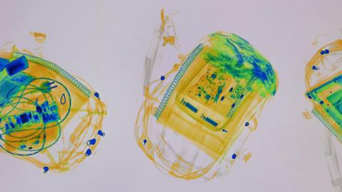 A colourful yellow, blue and green x-ray style image of backpacks being screened at an airport. 