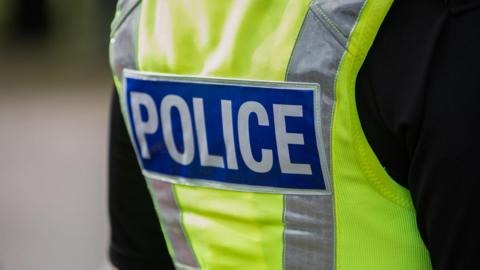 A close-up picture of the back of a police officer who is wearing a hi-vis reflective gilet.