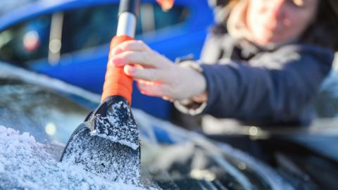 Woman deicing car windshield with ice scraper, selective focus