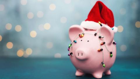 Piggy bank wearing a Christmas hat and decorated with fairy lights.