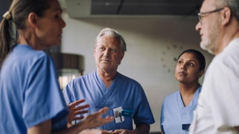 Two men and two women standing in a circle wearing medical scrubs. Stock Image