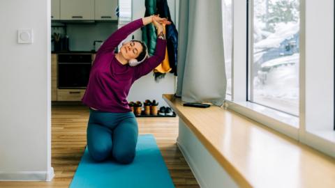 Woman practicing yoga in her apartment enjoying moment of relaxation with headphones - stock photo