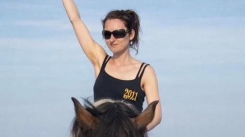 Naomi MacIvor is sitting on a horse and has an arm raised.