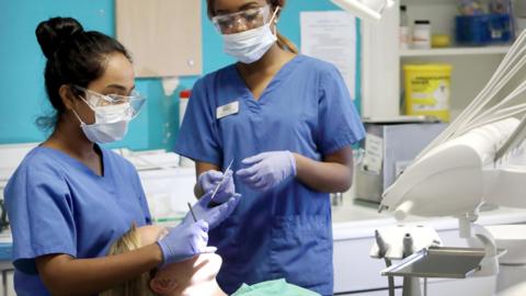 Young female dentist and assistant working on female patient in chair