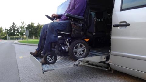 A wheelchair user getting out of a grey accessible taxi.