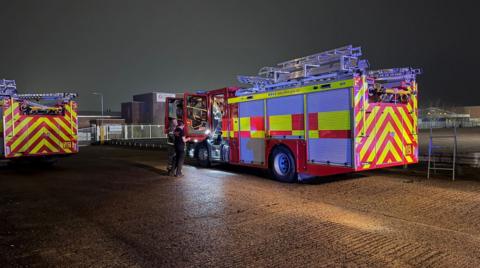 Two fire trucks parked on a road outside an industrial building
