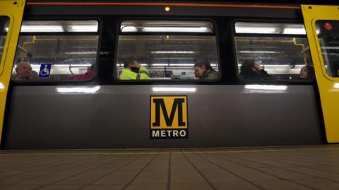 Passengers sitting on a Tyne and Wear Metro train as it sits at a station.