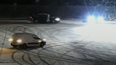 A screenshot of CCTV footage showing a white van doing doughnuts in a snow-covered car park.