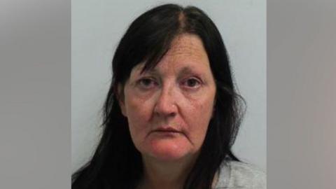 A police mug shot of Drina Gray, a woman with long dark hair