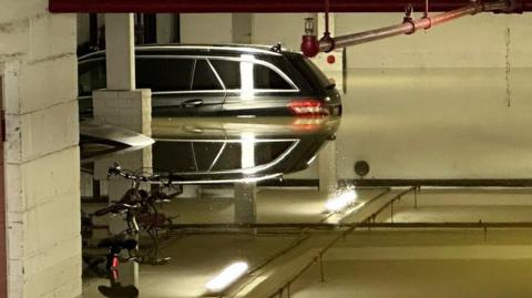 A flooded car park with the water level up to the break lights of two parked cars in the background. The rear brake lights are reflected in the water