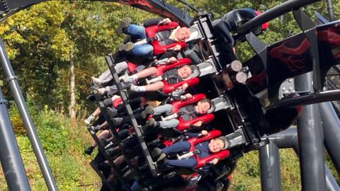 Children and an adult on a rollercoaster at the Alton Towers resort in Staffordshire. They appear to be smiling as the coaster makes its way around a sharp turn.