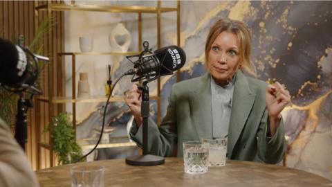 Vanessa Williams, wearing a pale green suit with light brown hair tied back, in front of a BBC Sounds microphone.