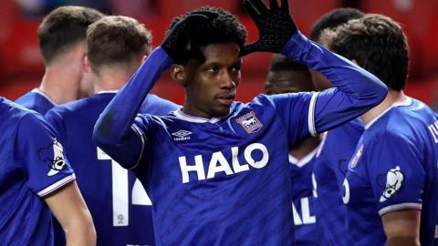 Jaden Philogene, wearing Ipswich's blue home shirt, puts his hands by his head to celebrate the winning goal at Charlton