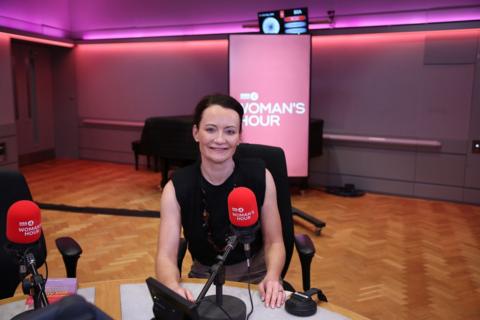 Dr Helen Wall smiles at the camera as she sits in front of a red BBC Woman's Hour microphone.