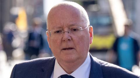 Peter Murrell, wearing a dark blue suit and tie and a white shirt