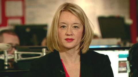 Maxine Hughes sitting in the BBC newsroom looking at the camera. She is wearing a red top and black blazer. 