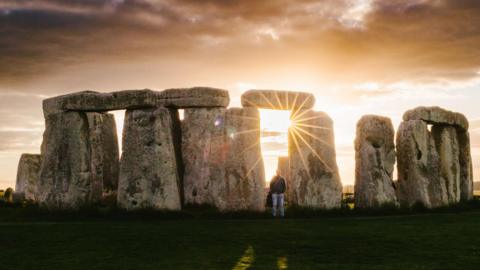 Man stands at Stonehenge with sunset and sunrays wonder - stock photo