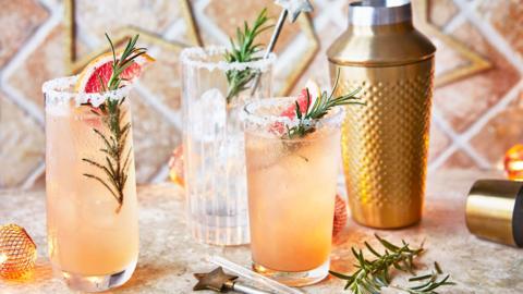 Glasses of orange, Paloma cocktails, decorated with sprigs of rosemary and grapefruit wedges.