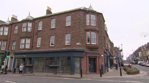 The front of the Three Frogs shop on the corner of Curzon Street and Senhouse Street, looking up towards other shops and businesses in the town.