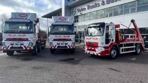 Three large white and red trucks, parked in front of an office building