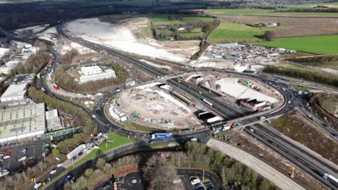 A drone view of the motorway junction over the M3 with construction areas, equipment and vehicles surrounding the various carriageways 