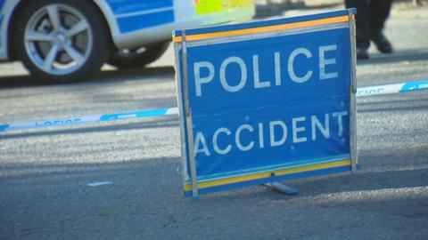 A blue police accident sign with police tape and a police car in the background