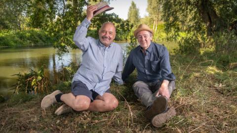 Bob Mortimer and Paul Whitehouse sitting by a lake in a woodland