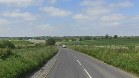 A long stretch of road in between two green fields