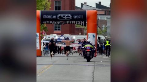 A runner with his hands raised and another runner coming up behind him 