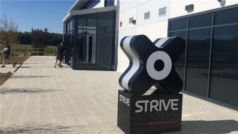 The exterior sign outside Strive Health Club which has black and white branding. The building has dark glass windows