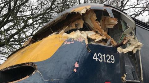 The badly-damaged cabin of a blue and yellow train