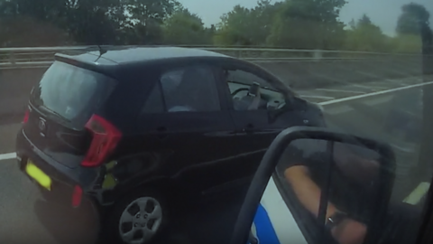 Small black car on a dual carriageway, driver seen holding mobile phone with open window as police officers stop her for the offence.