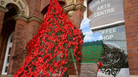 Exterior shot of Grantham Guildhall featuring a large outdoor display of red poppies and a silhouette artwork of a soldier.