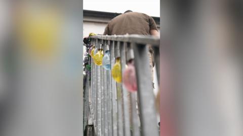 A man in a brown t-shirt stands at the top of a metal staircase