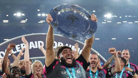 Big Zuu lifts the Soccer Aid trophy as World XI players celebrate their victory in 2025.