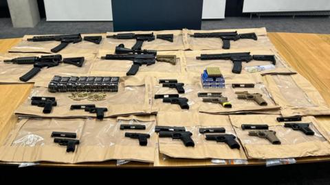 A number of firearms and ammunition laid out on display on a table