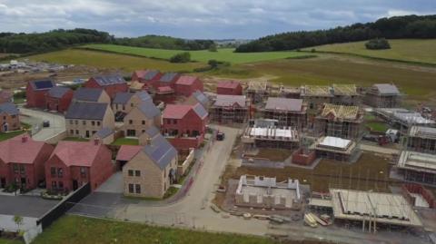 Drone view of a building site of houses being built with green fields in the background