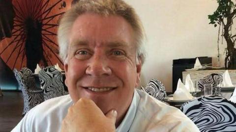 Close-up image of Philip Fryer. He has light grey hair and is wearing a light-blue shirt. He poses with his hand on his chin.