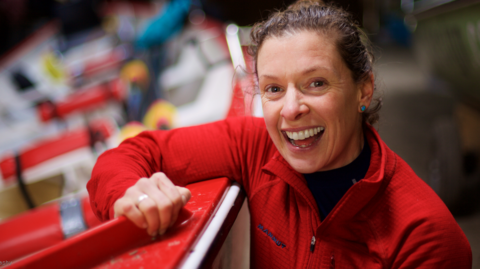 Kelda Wood, with her brown hair tied back and wearing a red fleece, smiling in a dark room