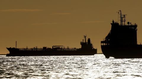 Silhouettes of two tankers on silver ocean water against a golden sunset