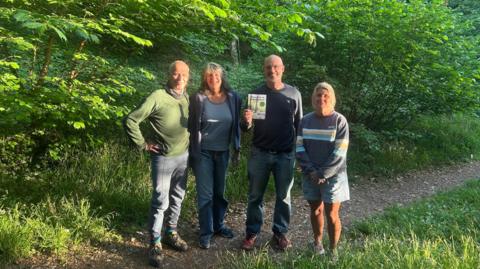A group of people, two men and two women standing in woodland. 