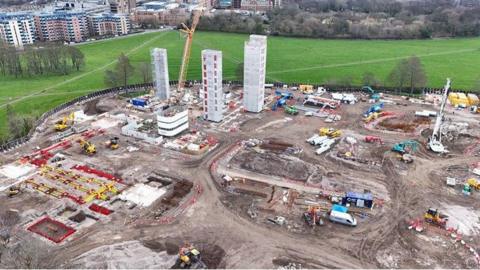 An aerial shot of building work for the Castle Leazes accommodation. The large site shows three core units of the building being erected with groundworks happening around the three shells, with lots of machinery and materials in the area. Outside the building site is a green area with more high rise buildings in the background.