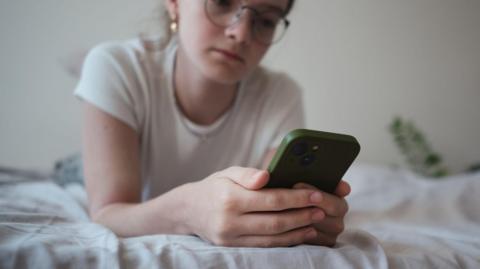 A teenager using her phone while lying on a bed.