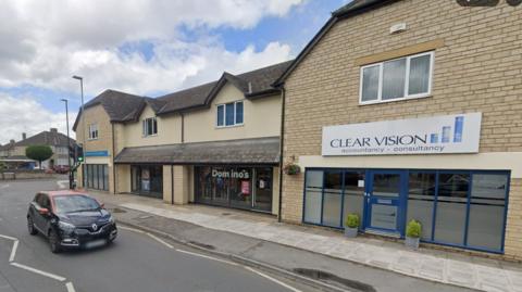 Newlands Road with a car driving towards the camera. A Dominos takeaway can be seen on the right in between two other shops.