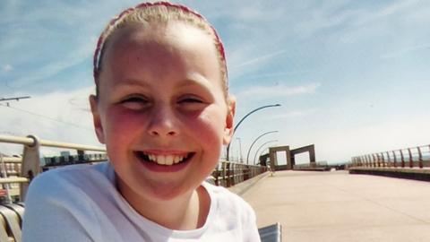 A young girl with a white top sits at a beach promenade