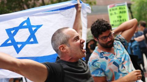 A pro-Israel demonstrator holds up an Israeli flag as Pro-Palestine protesters hold a rally against the Baruch College Hillel campus organization at Baruch College on June 05, 2024 in New York City